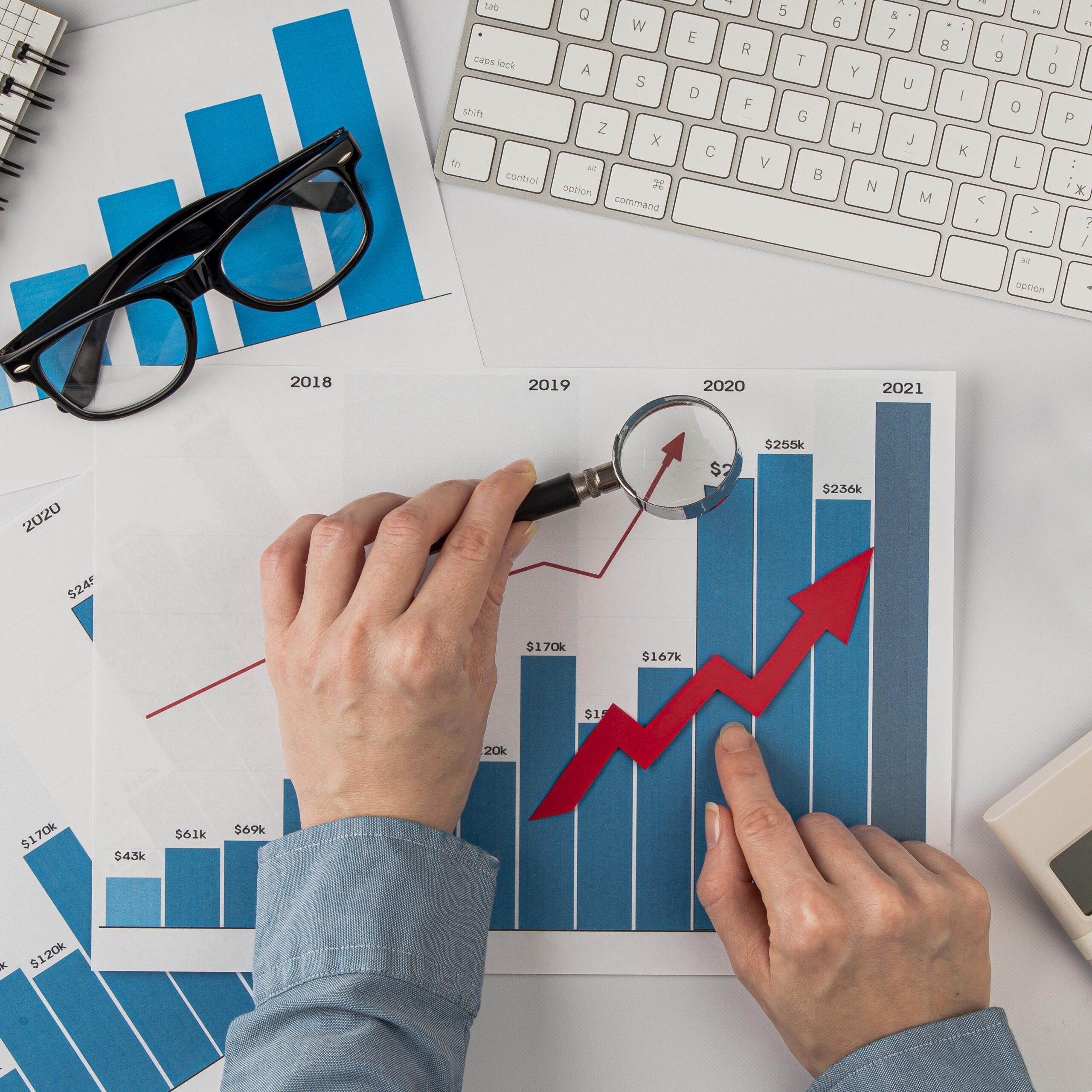 top-view-office-desk-with-growth-chart-hands-holding-magnifying-glass